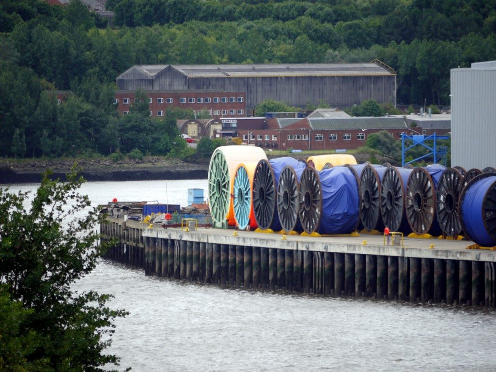 Holzkabeltrommeln mit aufgewickelten Unterseekabeln an einer Werft am Ufer